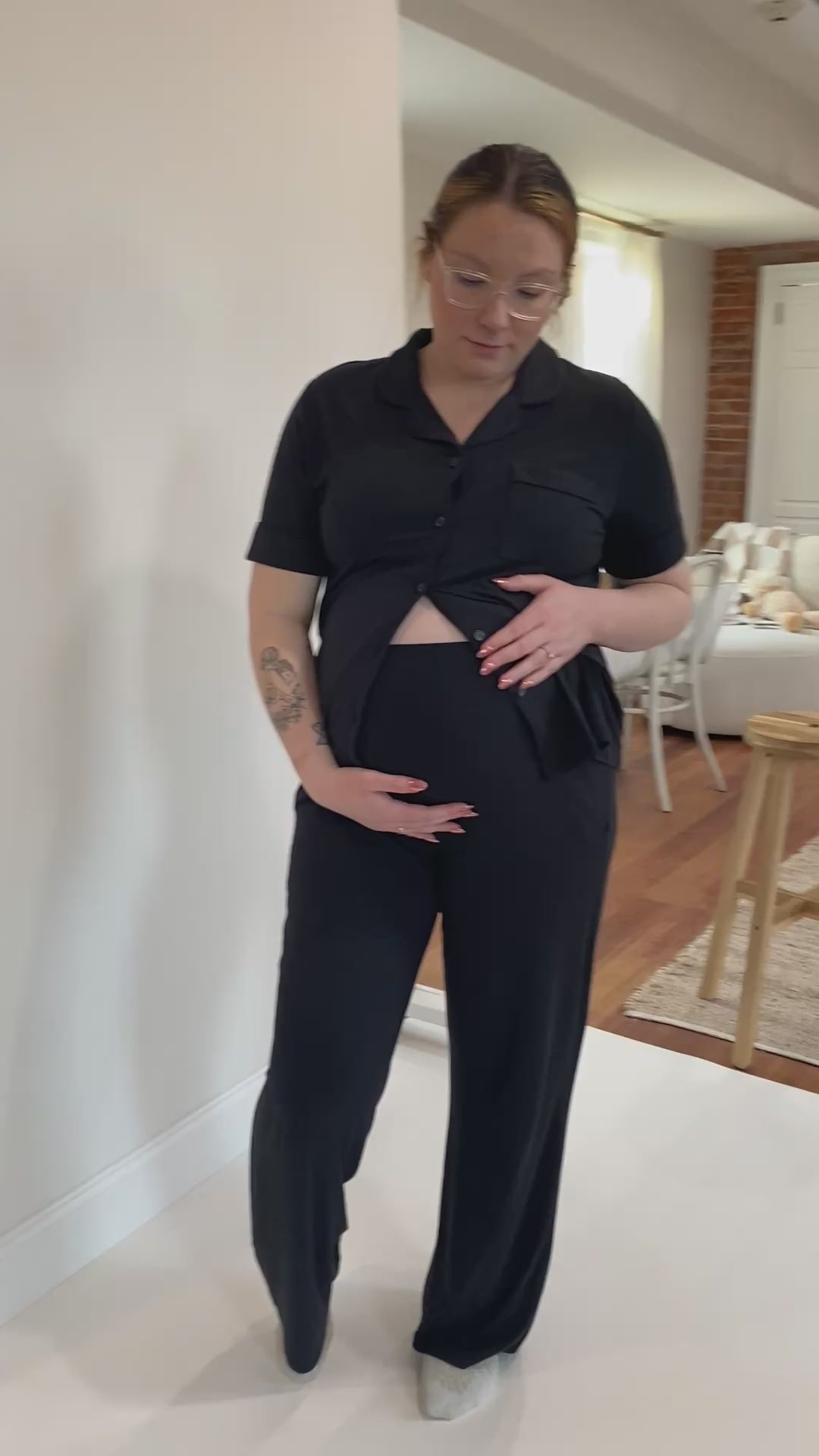 Load video: Pregnant woman in her third trimester wearing our pajamas in the classic maternity set, shade Midnight. Holding her belly, showing off the design of our high-waisted pajama bottoms, belly band.